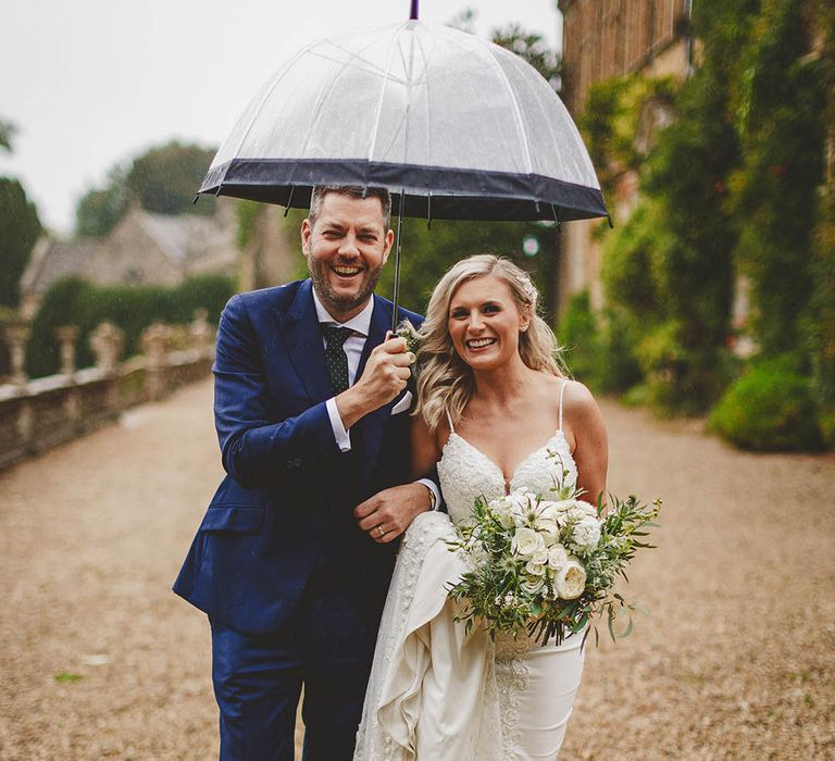 Win wedding photography with We Are // The Clarkes. This image showcases rain wedding photography with the Bride and Groom laughing under an umbrella