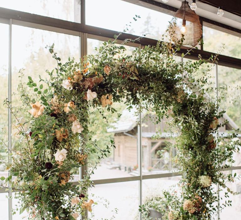 Floral moongate for wedding decoration with white, beige and dark coloured flowers with foliage 