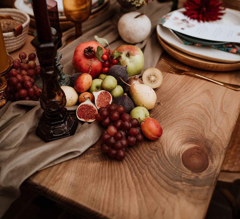 Seasonal fruit and vegetables decor on rustic autumnal wedding tablescape with large dark candlestick holders and dried flowers