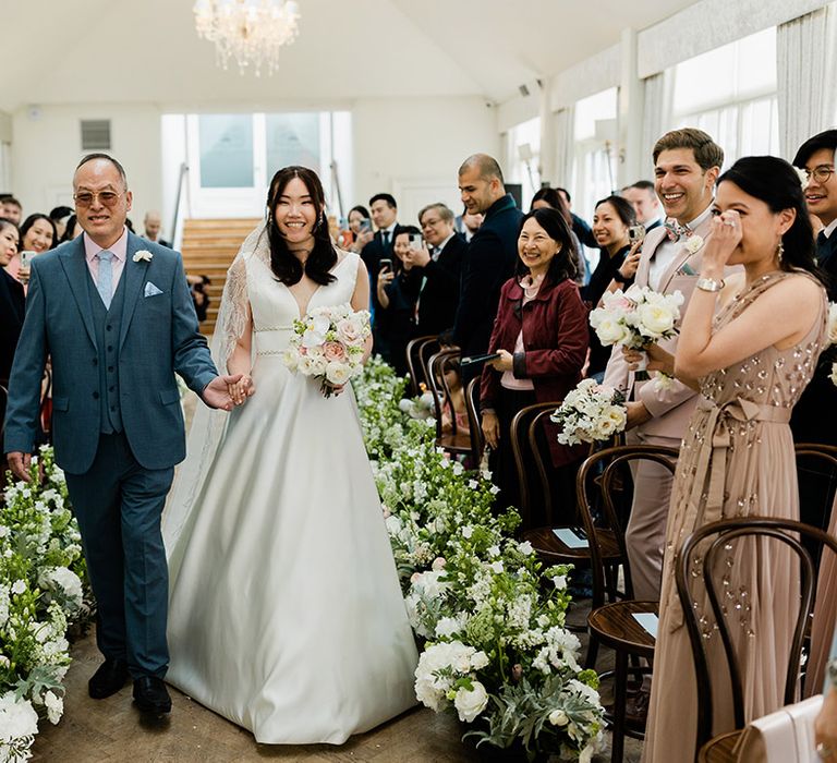 Bride in Princess wedding dress walks down the aisle with her father in power blue suit 