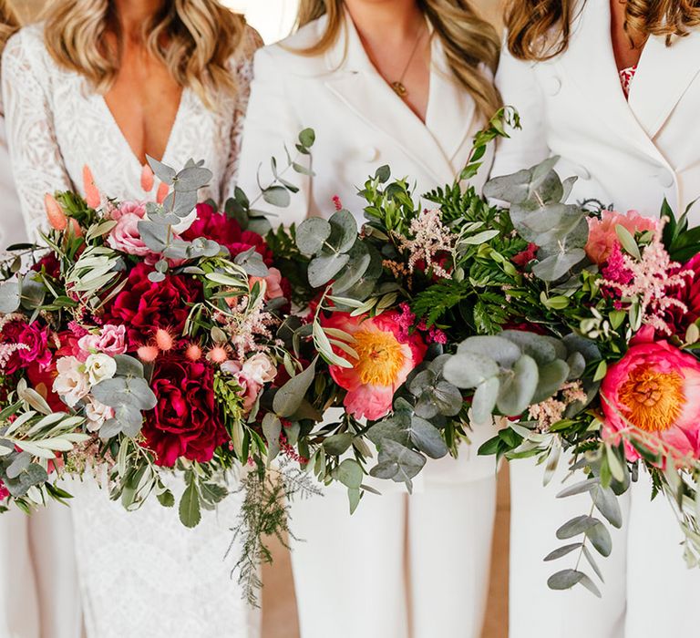 Bridesmaids in bridesmaid jumpsuits holding bouquets with red, pink and white garden roses, eucalyptus, foliage and dried flowers  