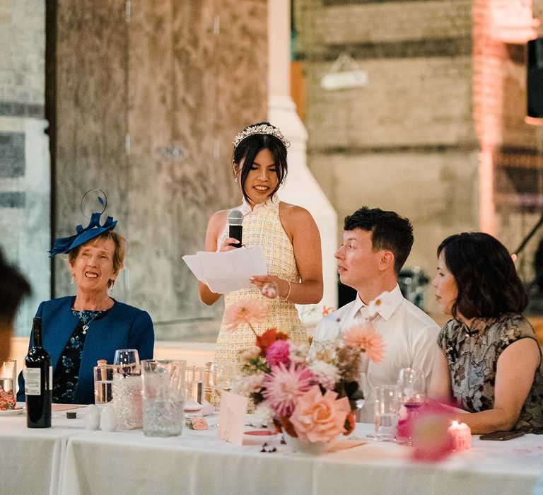 Bride wears high neck reception dress and feather embellished bridal crown during reception speech