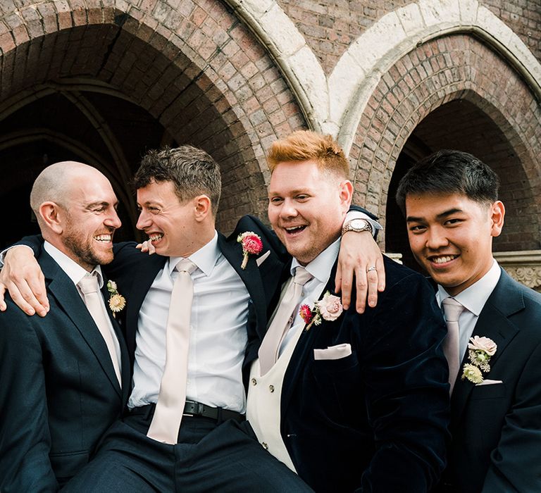 Groom in black suit and floral buttonhole is lifted by his groomsmen in different styled suits