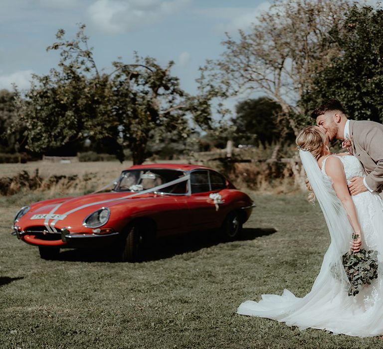 Groom kisses his bride beside red vintage wedding car 