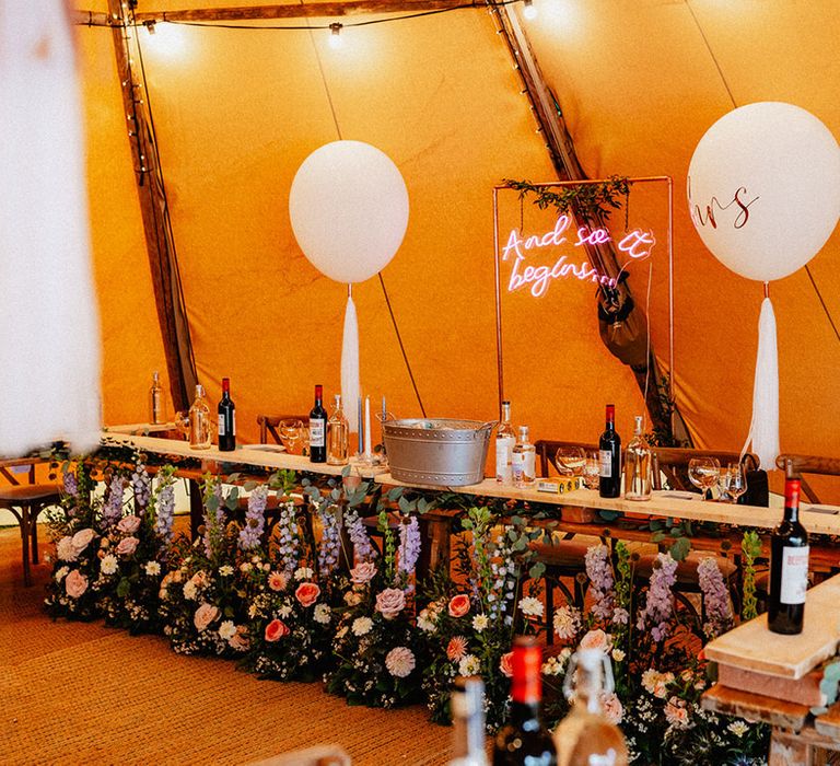 Tipi wedding reception with balloon wedding decor, neon lights and wildflowers decorating the top table 