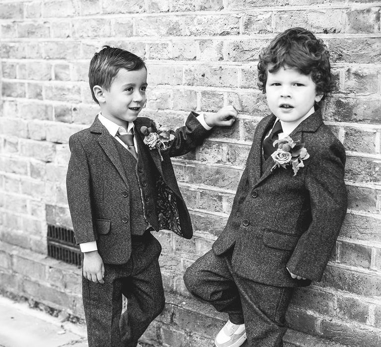 Page boys wearing matching textured three piece suits with rose and dried flower boutonnieres and white trainers 