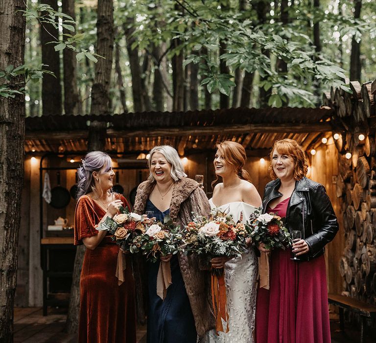 Bride stands beside her bridesmaids in mismatched Autumnal bridesmaid dresses with dried floral bouquets 