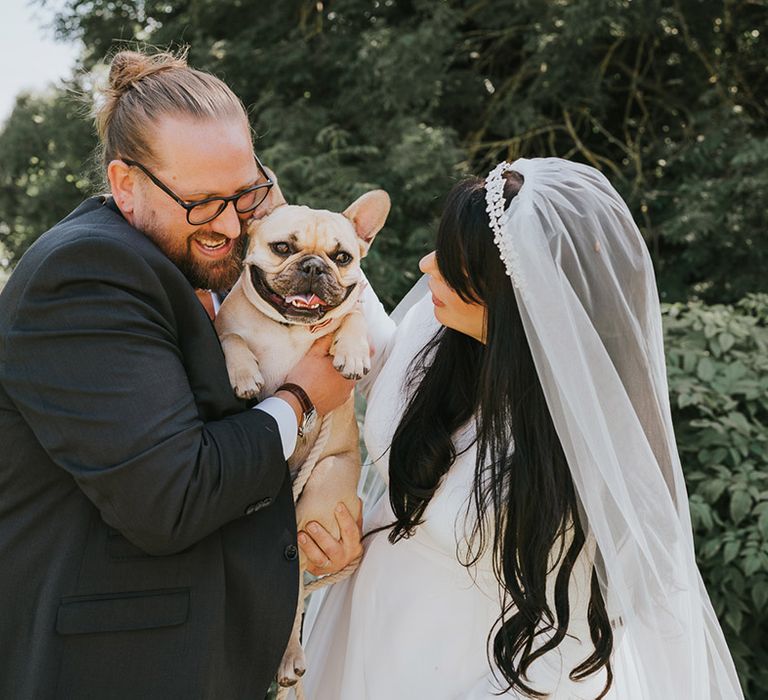 The bride in a high neck long sleeve dress with the groom in a dark grey suit giving love to their dog, Stitch