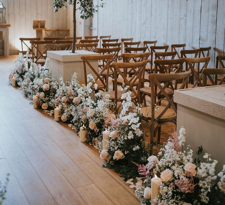 Rows of wedding flowers with pink roses, gypsophila, and pink grass with pillar candles 