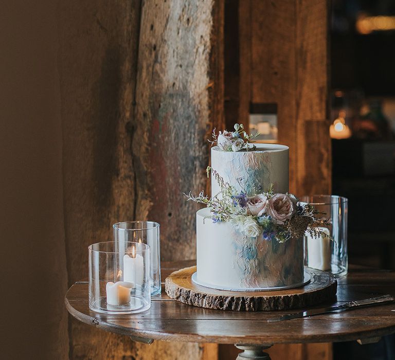 two tier wedding cake on a tree slice with pastel design and wedding flowers 