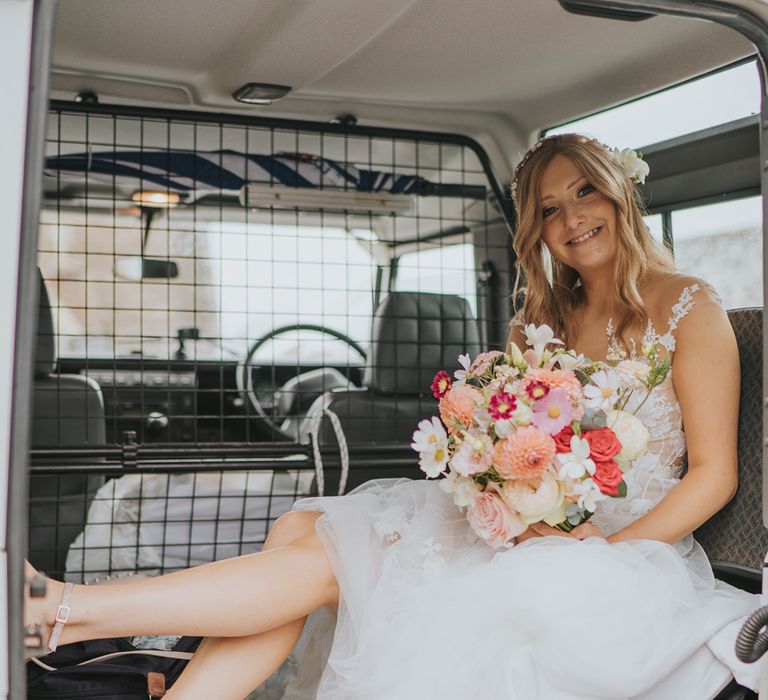 Bride in Anna Kara wedding dress holding pastel flower wedding bouquet with sparkly shoes in wedding car 