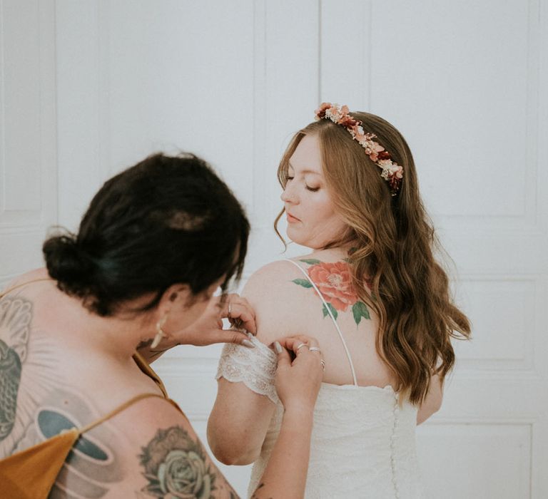 wedding morning bridal preparations with bridesmaid helping the bride into her lace wedding dress