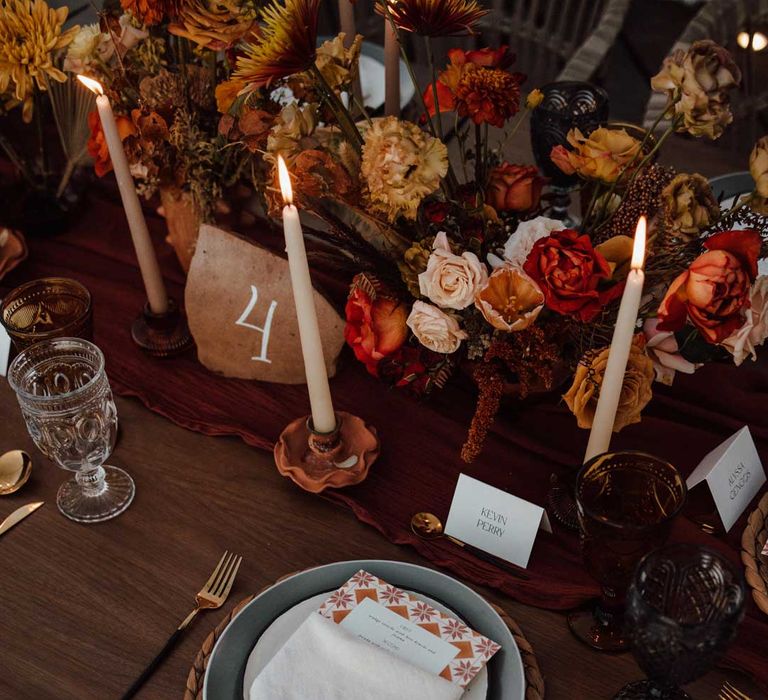 Rustic wedding tablescape with burnt orange dried roses, dried flower and foliage floral centrepieces, wooden slate wedding table numbers, light orange tapered candles and burnt orange table runners