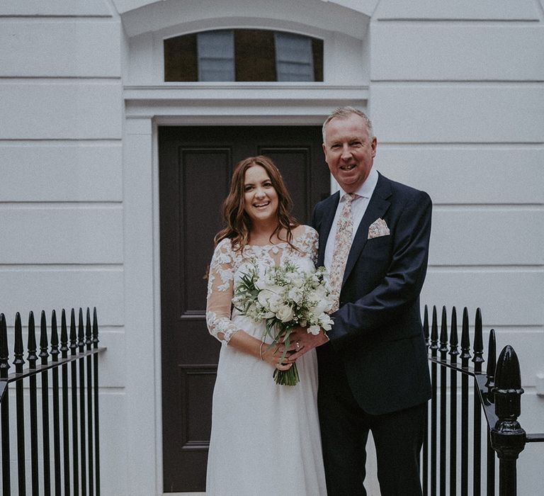 Pregnant bride in lace maternity wedding dress holding white wedding bouquet with the father of the bride in dark suit with floral tie 