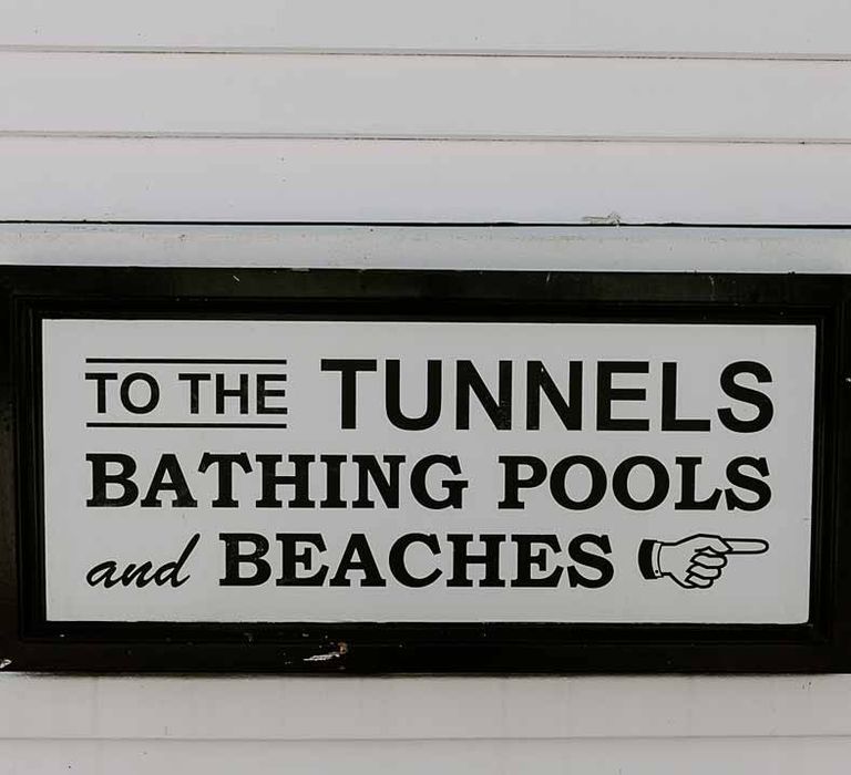 Black wedding sign at Tunnels Beaches directing guests to the bathing pools and beaches 