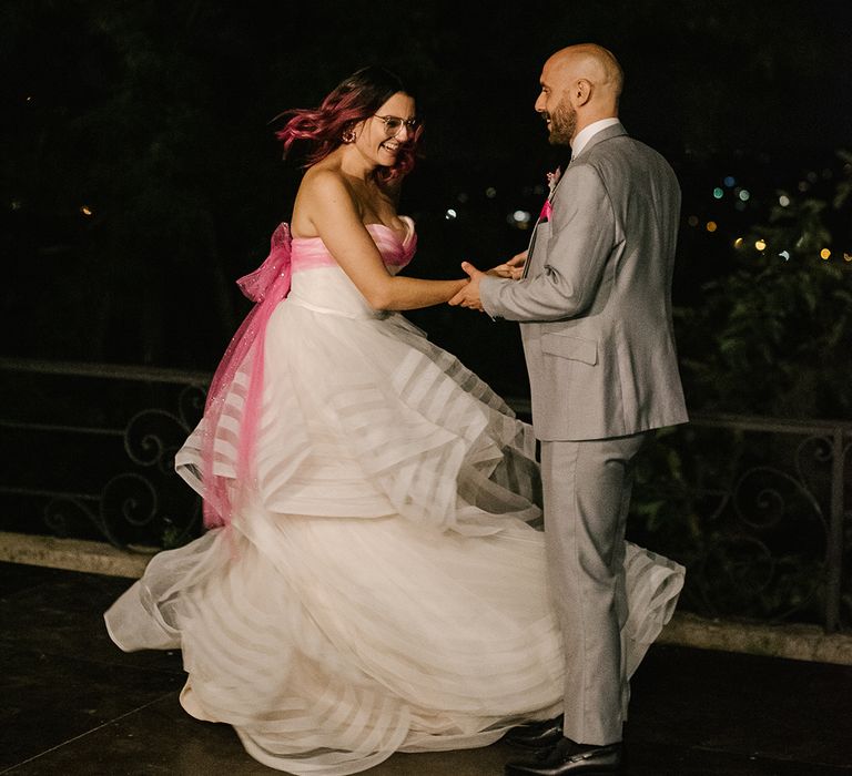 first dance with bride in a strapless layered wedding dress with pink bow and groom in a grey suit