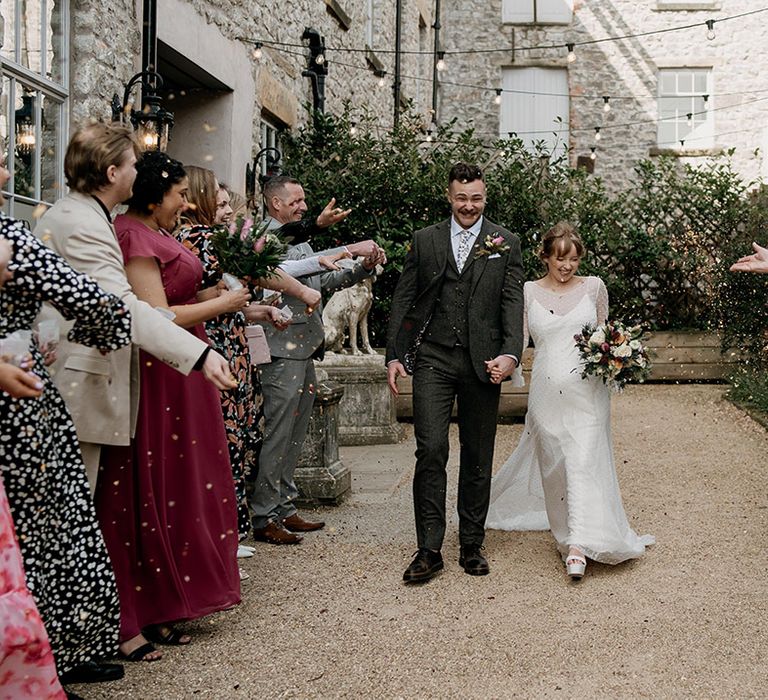 The bride in a polka dot print wedding dress has confetti moment with groom in grey suit 