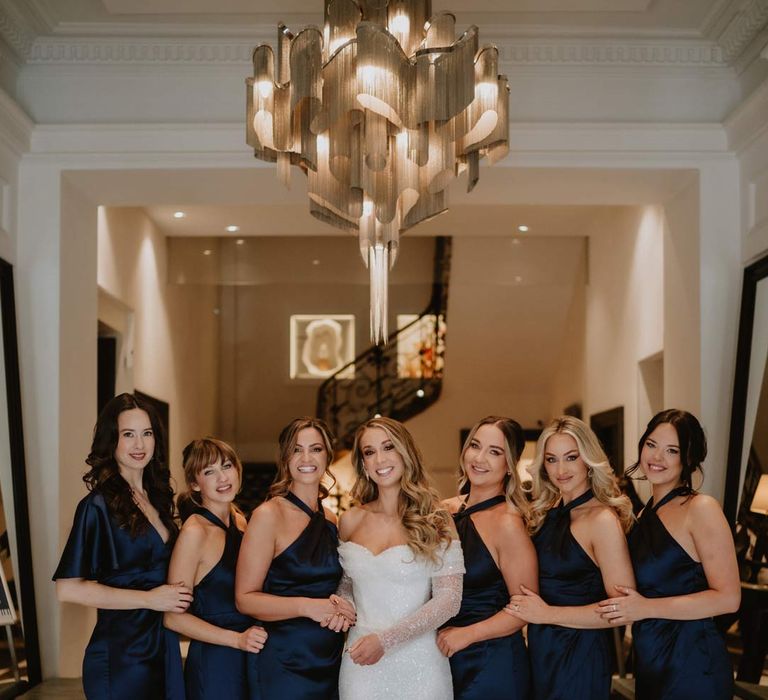 Bride in off shoulder sparkly mermaid wedding dress standing with bridesmaids in satin halterneck navy bridesmaid dresses in La Cabane Des Praz ski wedding