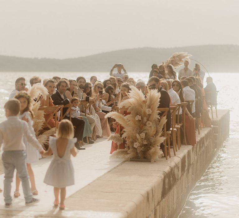 flower girls and page boys walking down the aisle at Croatia coastal wedding with pampas grass aisle wedding ceremony flowers 