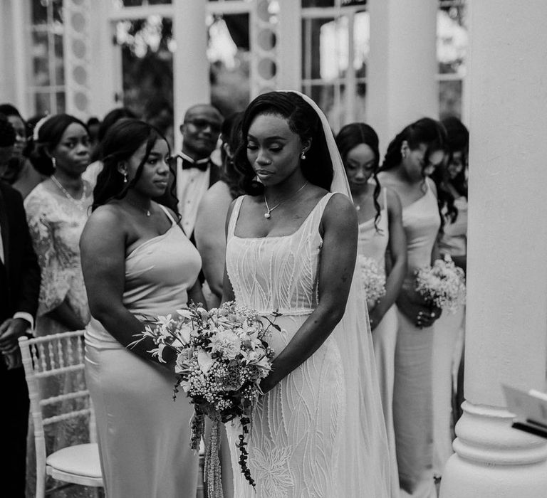 The bride wears a fitted beaded wedding dress as she stands at the altar 