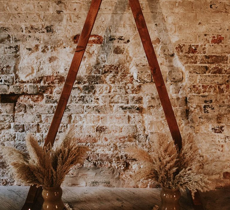 Wooden arch altar decoration with pampas grass and pillar candles DIY'd by the bride and groom 