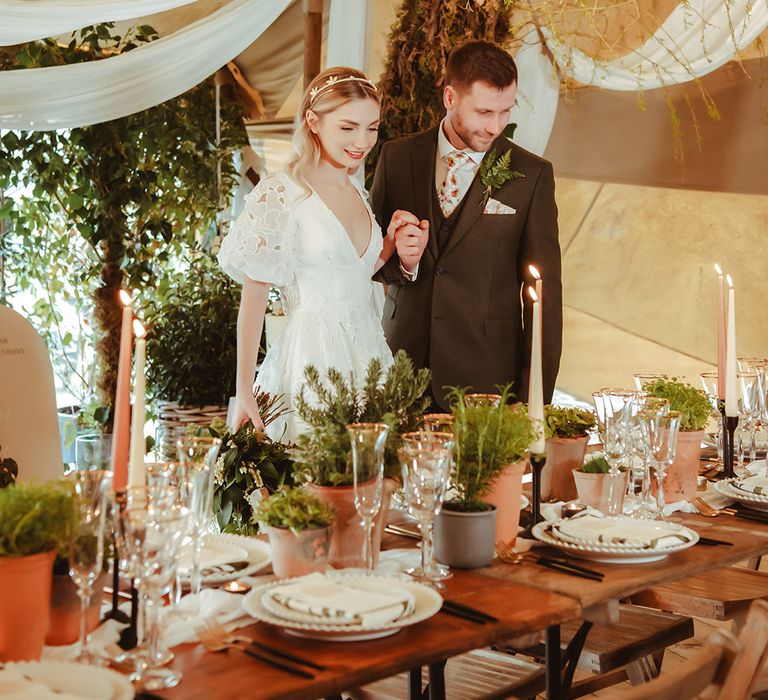 White drapery decorations at The Garden Tipi wedding venue with lots of natural foliage with the bride in floral lace wedding dress and groom in brown wedding suit 