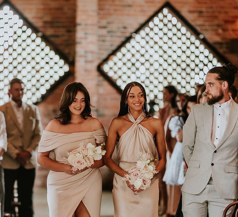 Bridesmaids in mismatched champagne coloured neutral bridesmaid dresses walking down the aisle together 