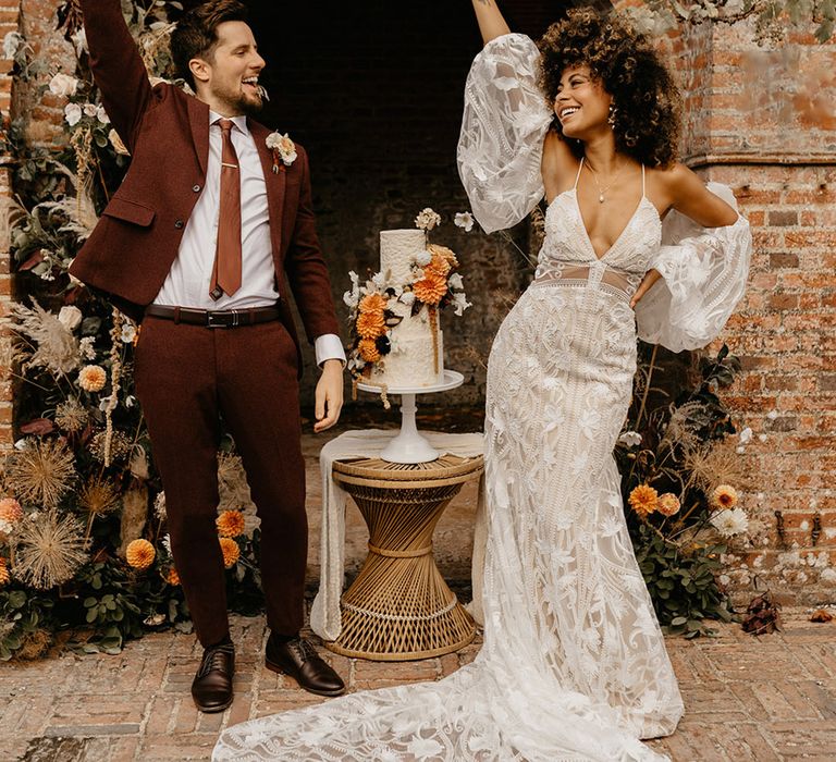 Bride in boho wedding dress with detachable sleeves smiling and celebrating with the groom in a red wedding suit for wedding in Kent 