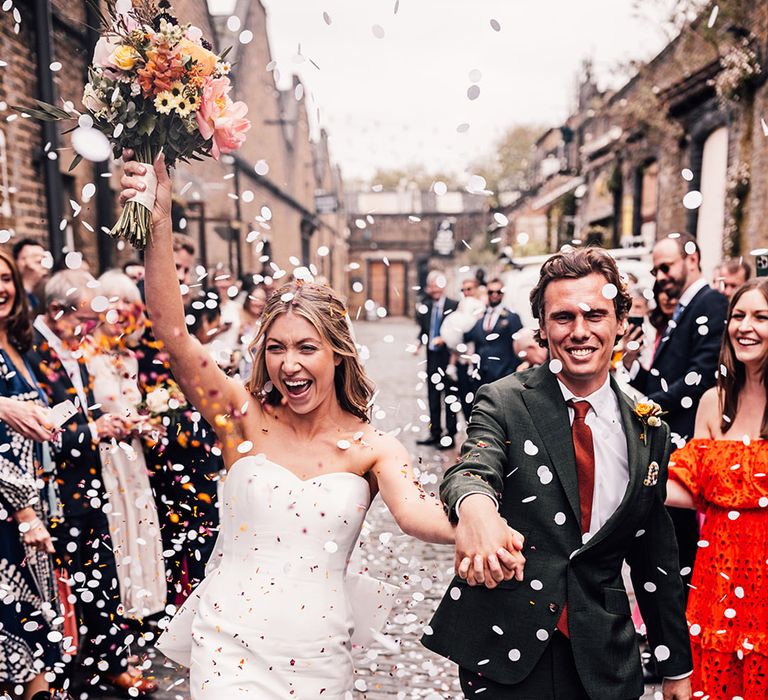 Bride in strapless gown with the groom in dark green suit with orange tie have confetti moment 