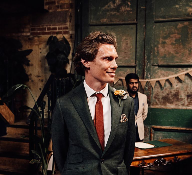 The groom wears a dark green wedding suit with an orange tie at the wedding with houndstooth pocketsquare 