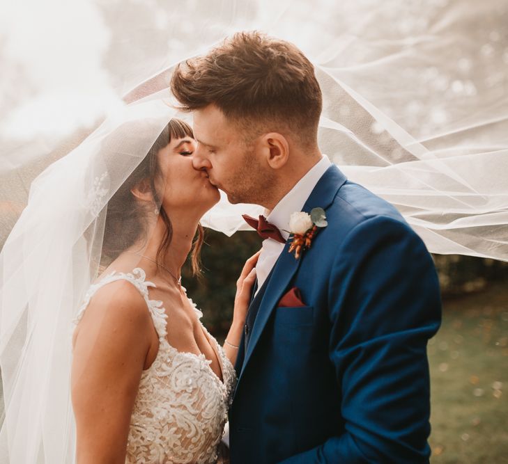 Bride and groom kissing with wedding veil blowing in the wind