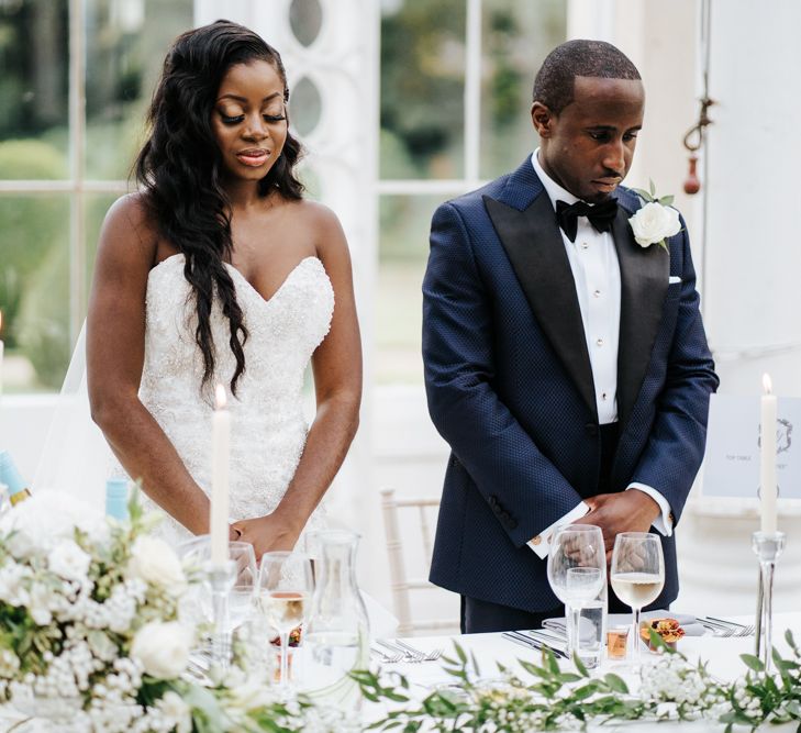 Bride and groom saying a prayer standing at their sweetheart table 