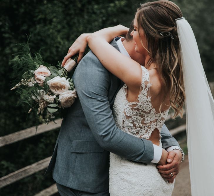 Groom embracing his bride in a lace back wedding dress