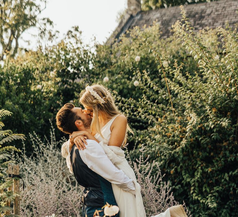 Groom picks up bride in satin wedding dress and lace cardigan with wedges 