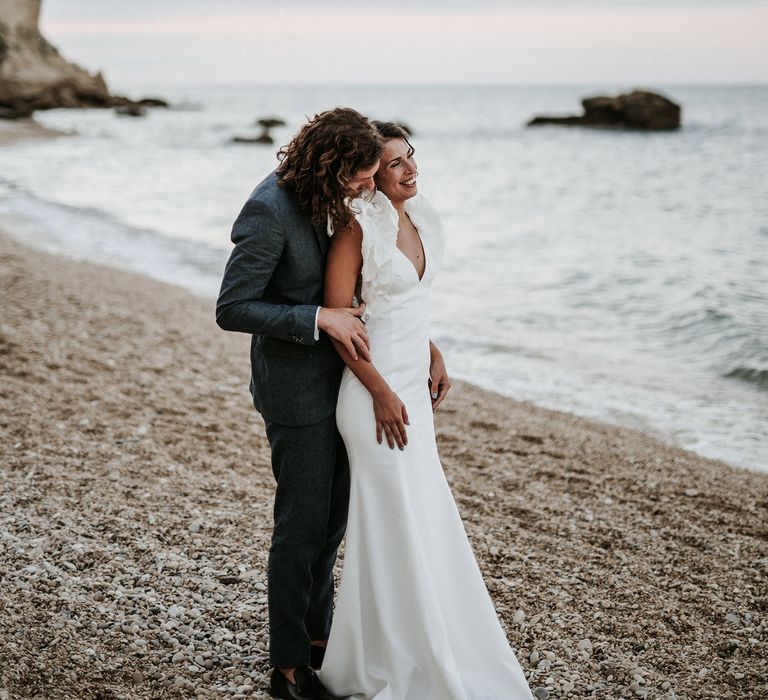 Bride and groom portrait on the beach with bride in a fitted Rime Arodaky wedding dress with ruffle sleeves and groom in a navy blue suit