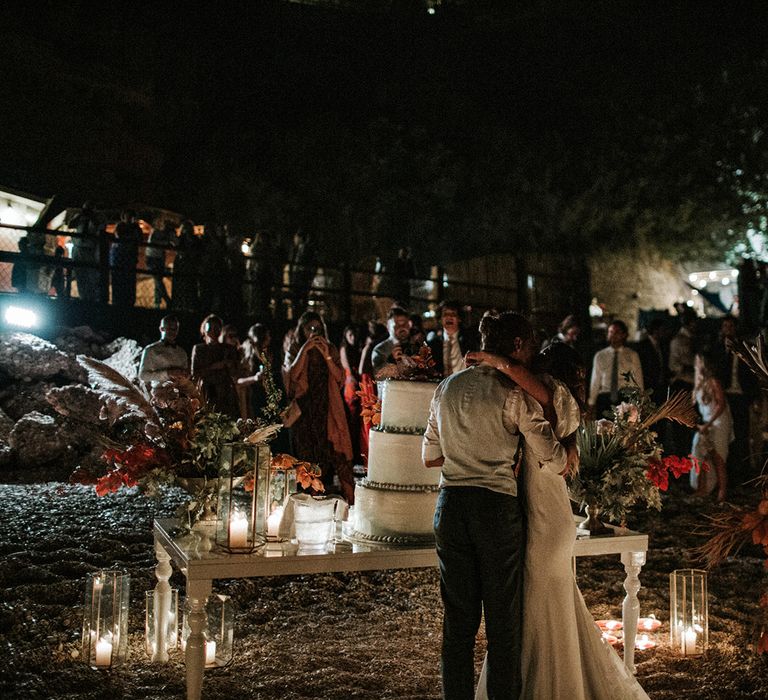 Bride and cutting their wedding cake on the beach with lanterns and dried flower decor 