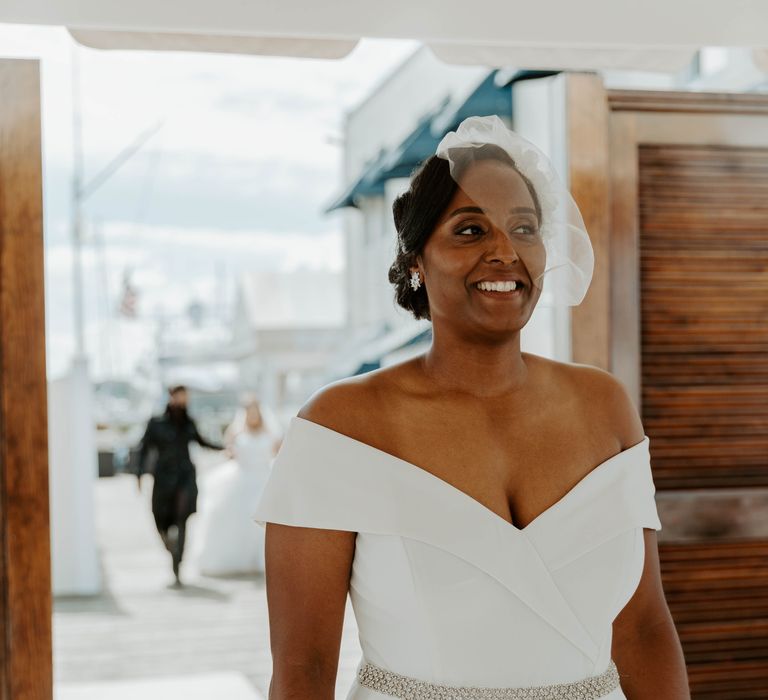 Black bride in off the shoulder jumpsuit with jewel belt detail and blush veil waiting for her bride for the first look 