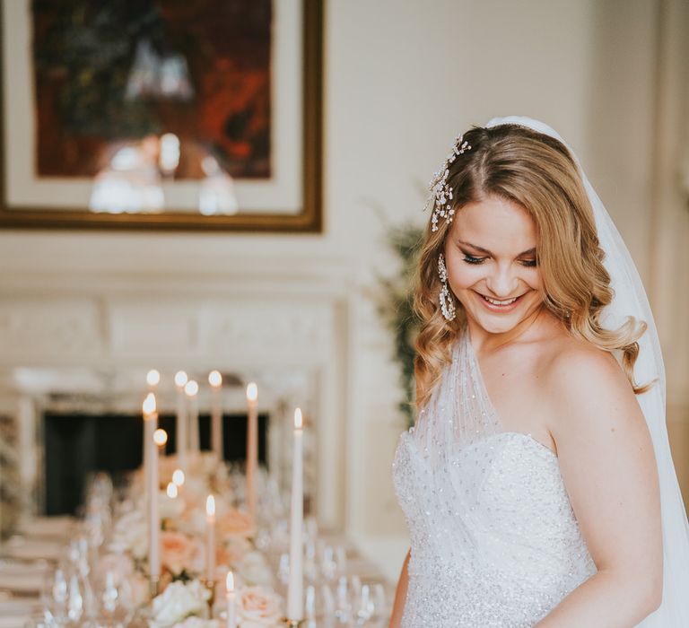 Bride in a one shoulder sparkly wedding dress standing next to her reception table with taper candles and floral arrangements 