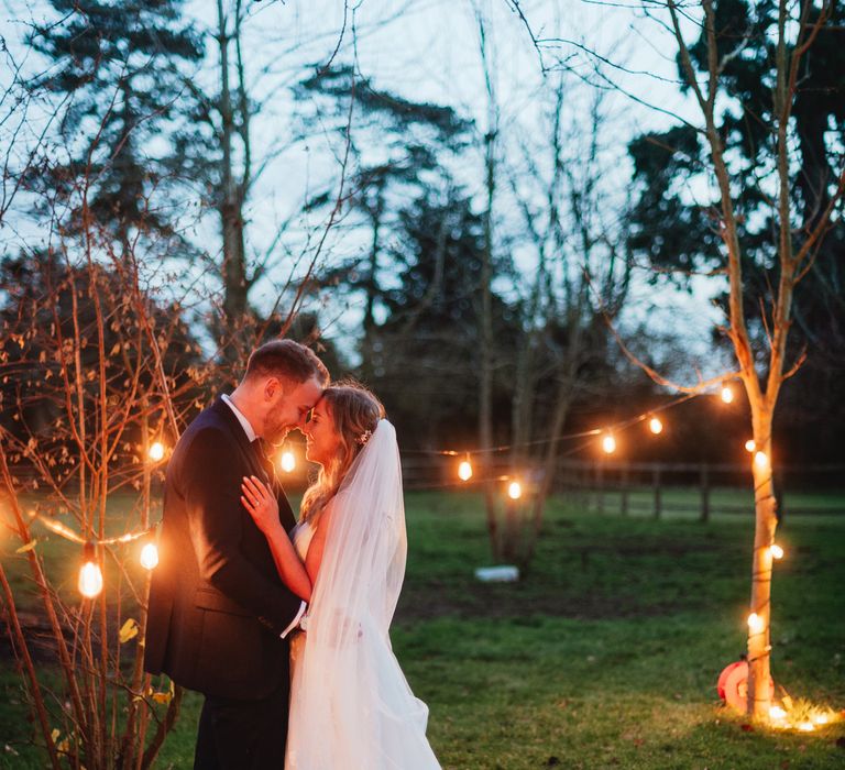 Bride & groom stand together outdoors surrounded by lights