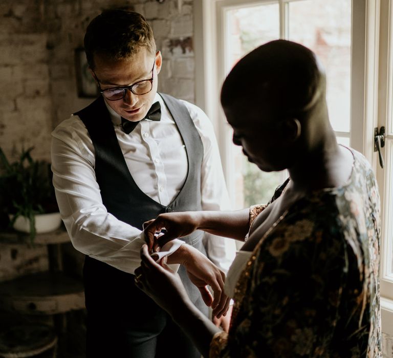 Black bride with alopecia helping her groom put on his cufflinks on the wedding morning 