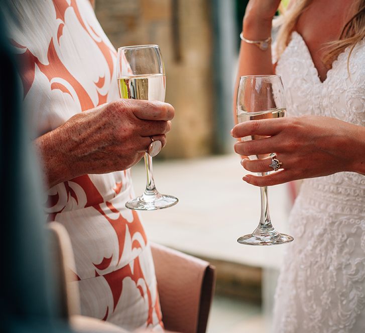 Bride holding champagne standing with wedding guest wearing lace bridal gown