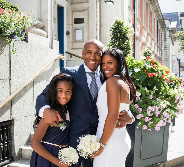 Family portrait outside Chelsea Town Hall with bride in a one shoulder Roland Mouret dress holding a white rose and gypsophila bouquet 