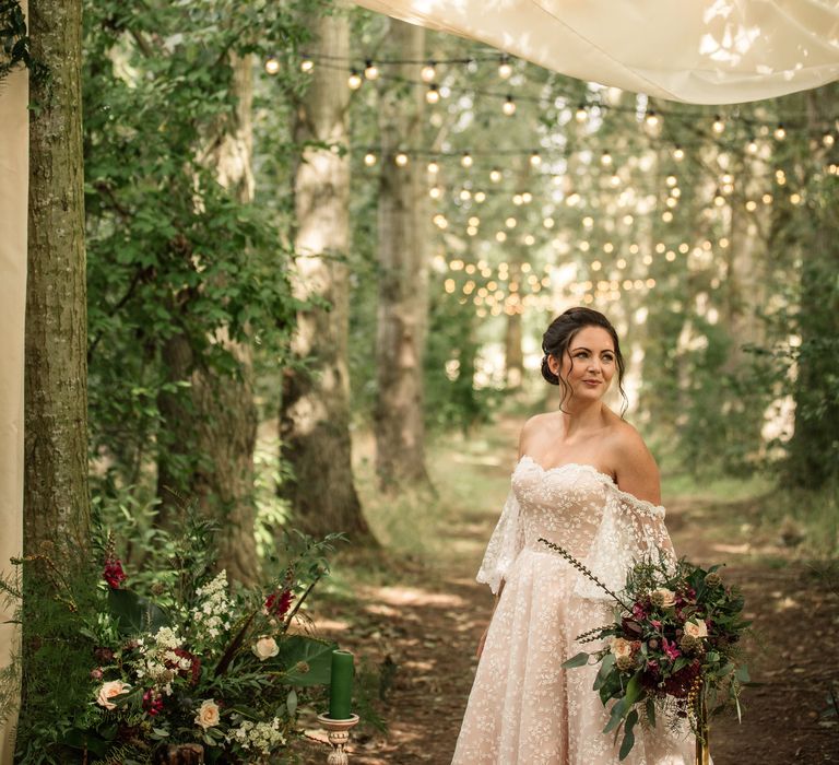 Bride stands under fairy lit line of trees