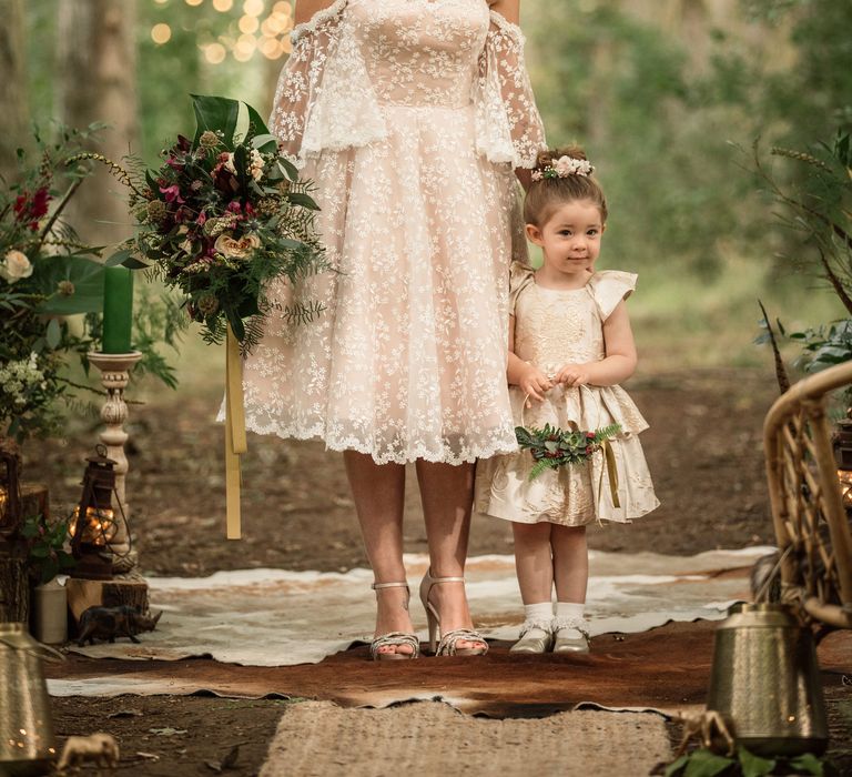 Bride stands with little girl whilst holding floral bouquet