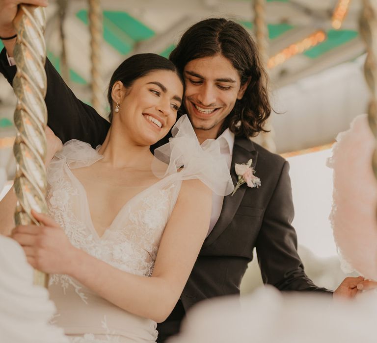 Bride in a fitted lace wedding dress with plunging neckline and chiffon shoulder detail riding the carousel at Preston Court 