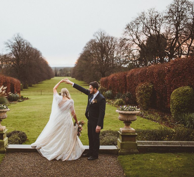 Groom in wedding tails twirling his bride in a princess wedding dress and cape at Goldsborough Hall wedding venue 