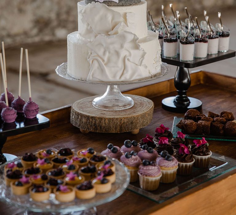 Dessert table with iced wedding cake in glass stand with two wooden brides as the cake topper 