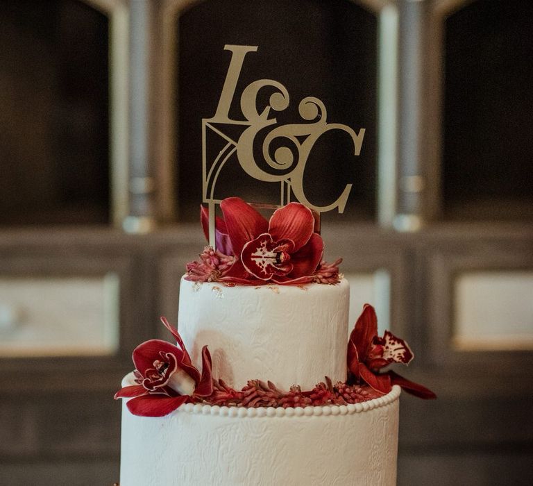 Two tier iced white wedding cake with red orchid decoration and 'L&C' cake topper