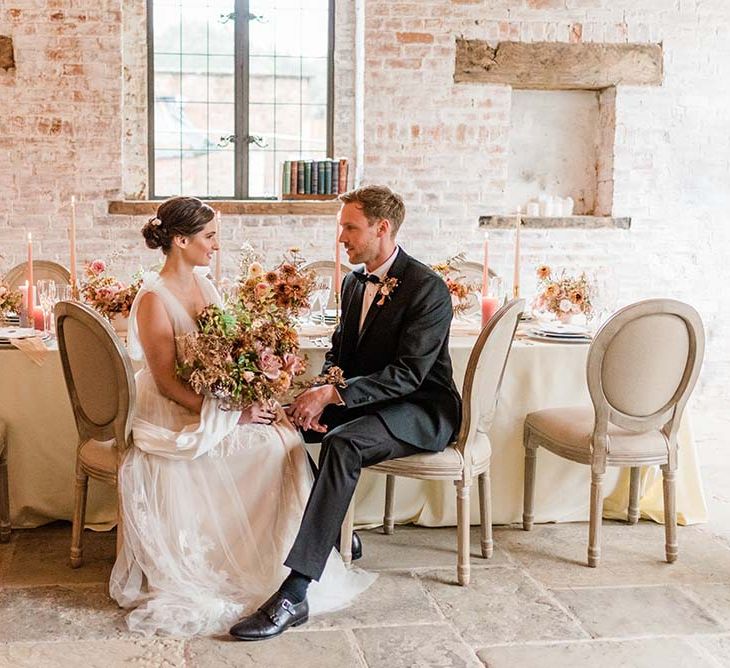 Bride and groom sitting at their intimate tablescape with 8 place settings, candles and autumn flower arrangements 