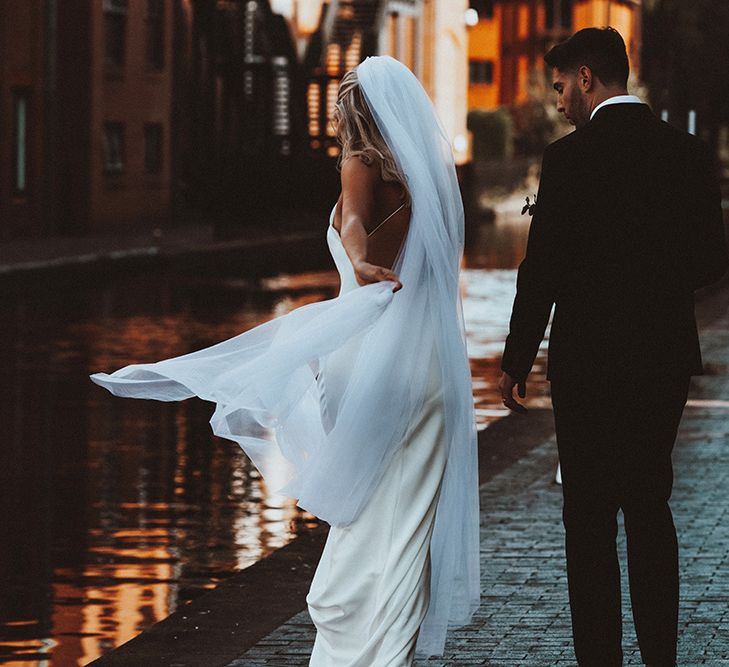 Bride in a slip wedding dress with cross over back detail and cathedral length veil blowing in the wind 